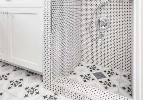 A pet wash station in a renovated laundry room with white cabinets, patterned tiles, and a chrome faucet.